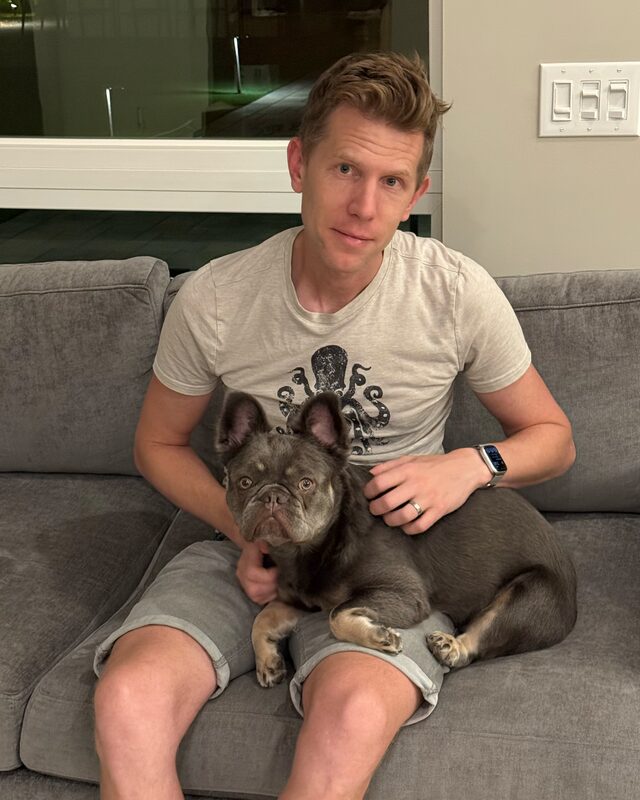 Tim on a grey sofa with Hermes curled in his lap