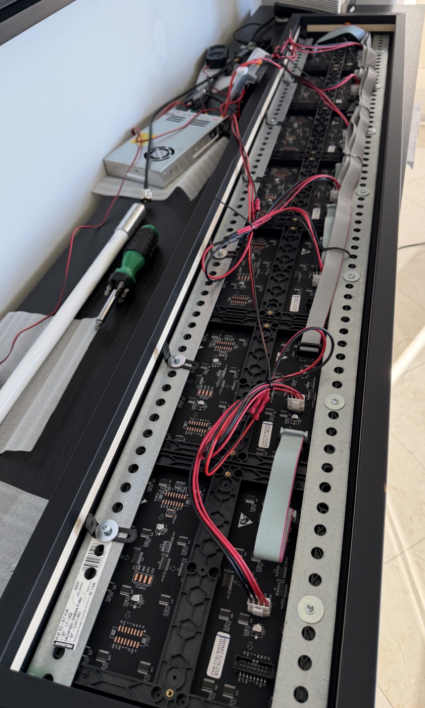 The back of the frame during the build: panels on a rail, red and black power pairs and grey ribbon cables, the power supply at the top